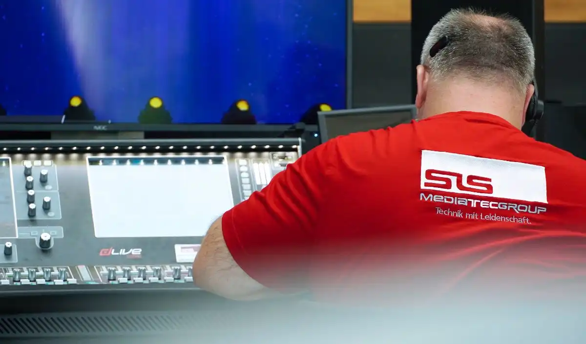 Betreuung-1-1 Eine Person in einem roten SLS-Mediatecgroup-Shirt bedient ein großes Mischpult, während auf einem Bildschirm vor ihr die Bühnenbeleuchtung zu sehen ist.